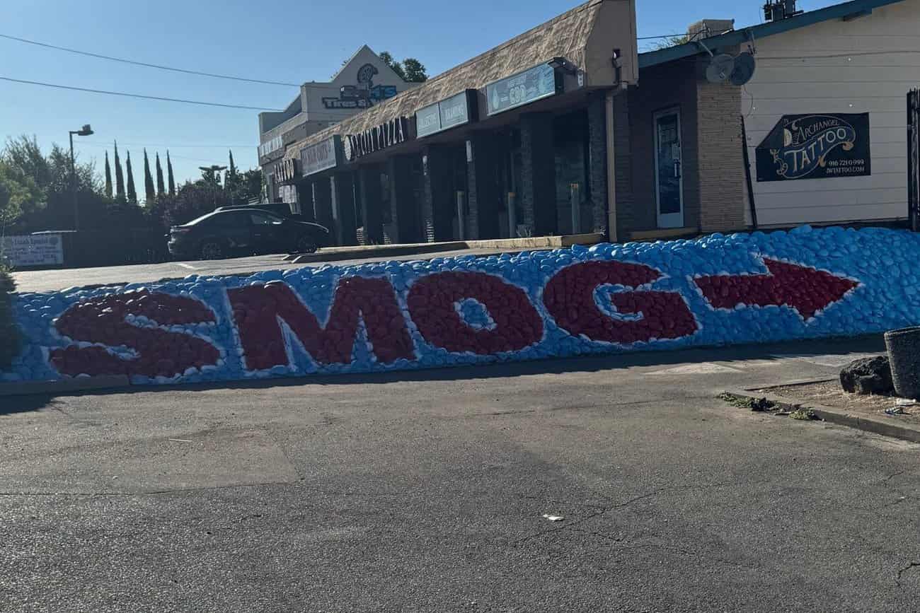 Wide view of the SMOG rock wall in front of the plaza storefronts, its red arrow pointing toward the back lot