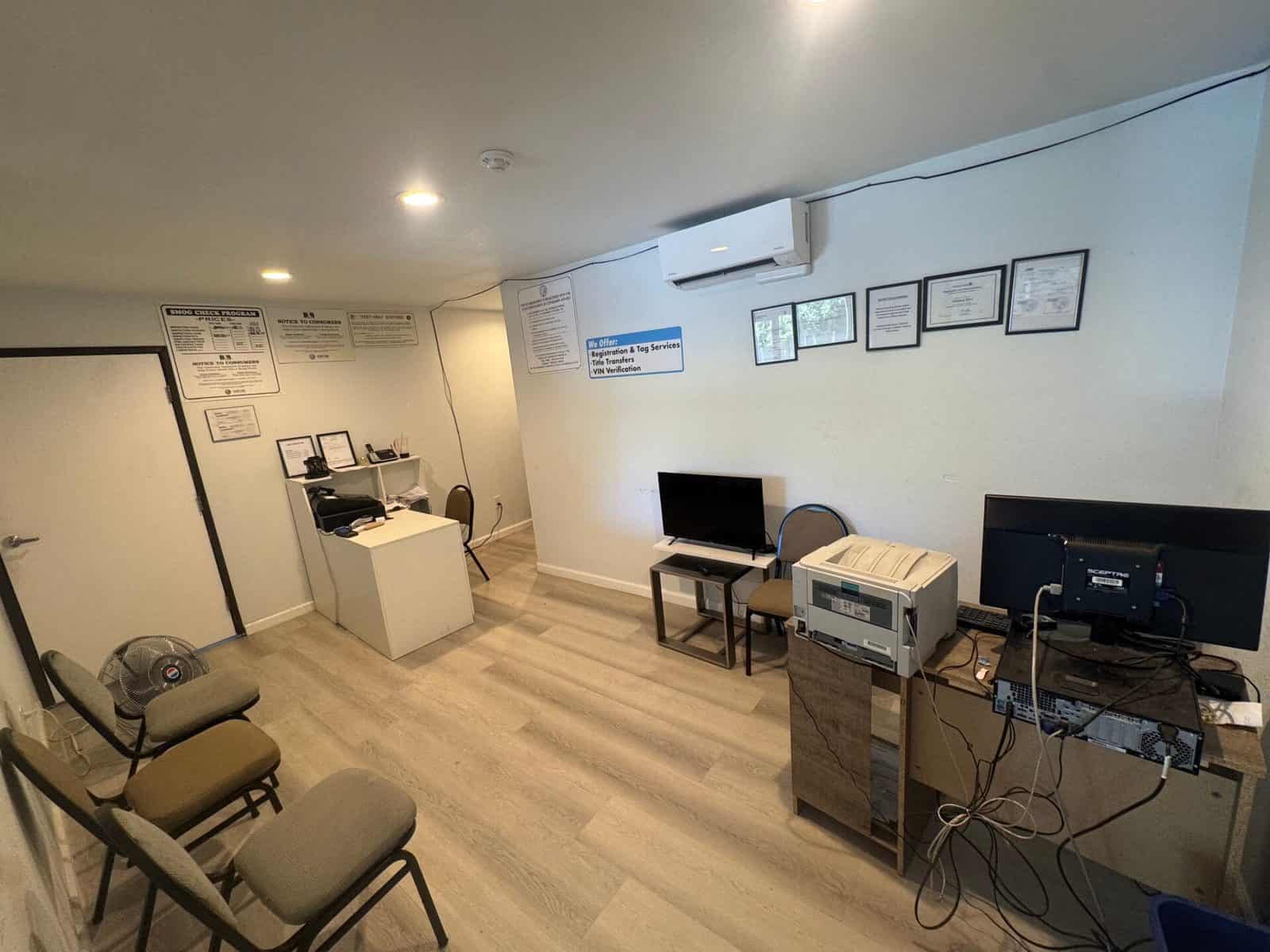 Waiting area with chairs, a television, and a wall sign listing registration and tag services, title transfers, and VIN verification