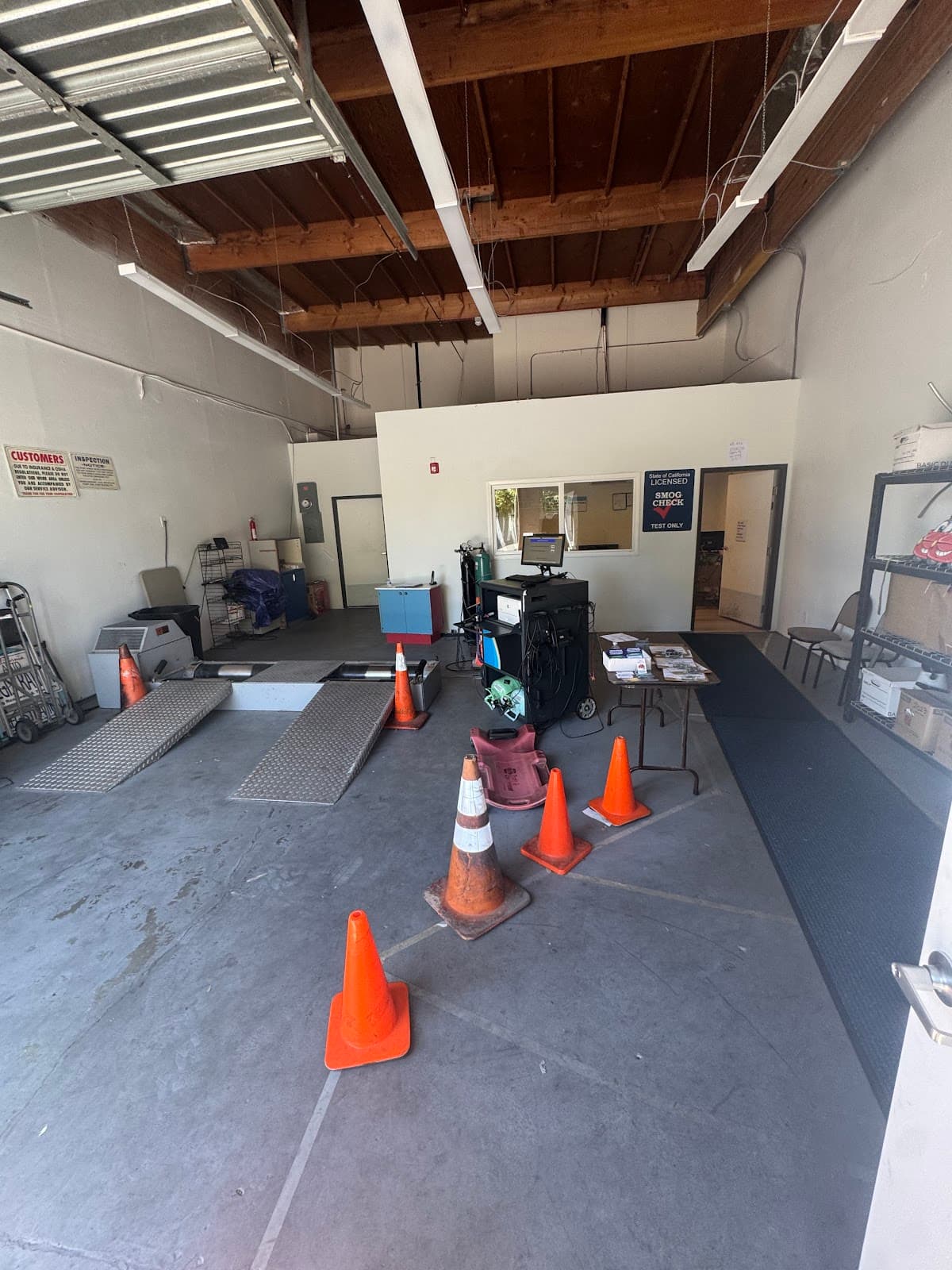 Inside the shop's inspection bay with drive-on ramps, traffic cones, and the licensed smog check sign
