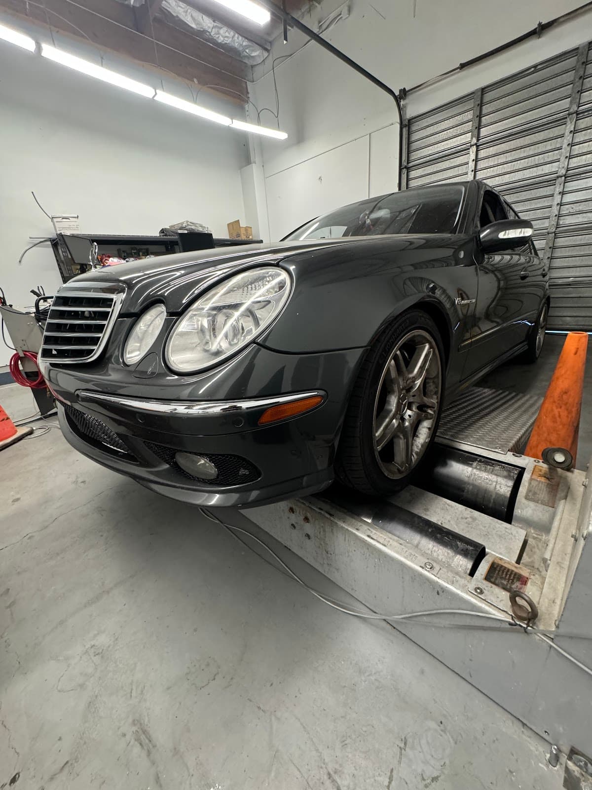 Dark grey Mercedes sedan on the dynamometer rollers in the shop's inspection bay