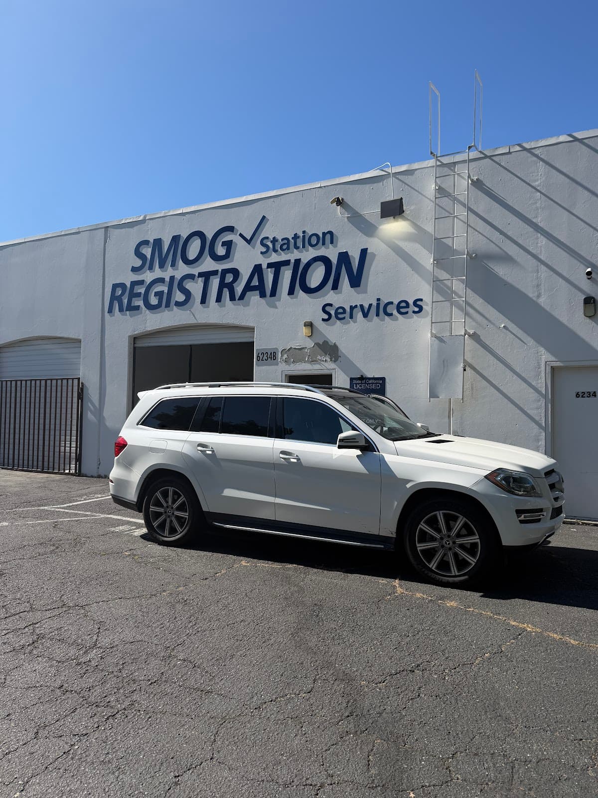 White Mercedes SUV parked outside unit 6234B, beneath the SMOG Station Registration Services lettering on the building