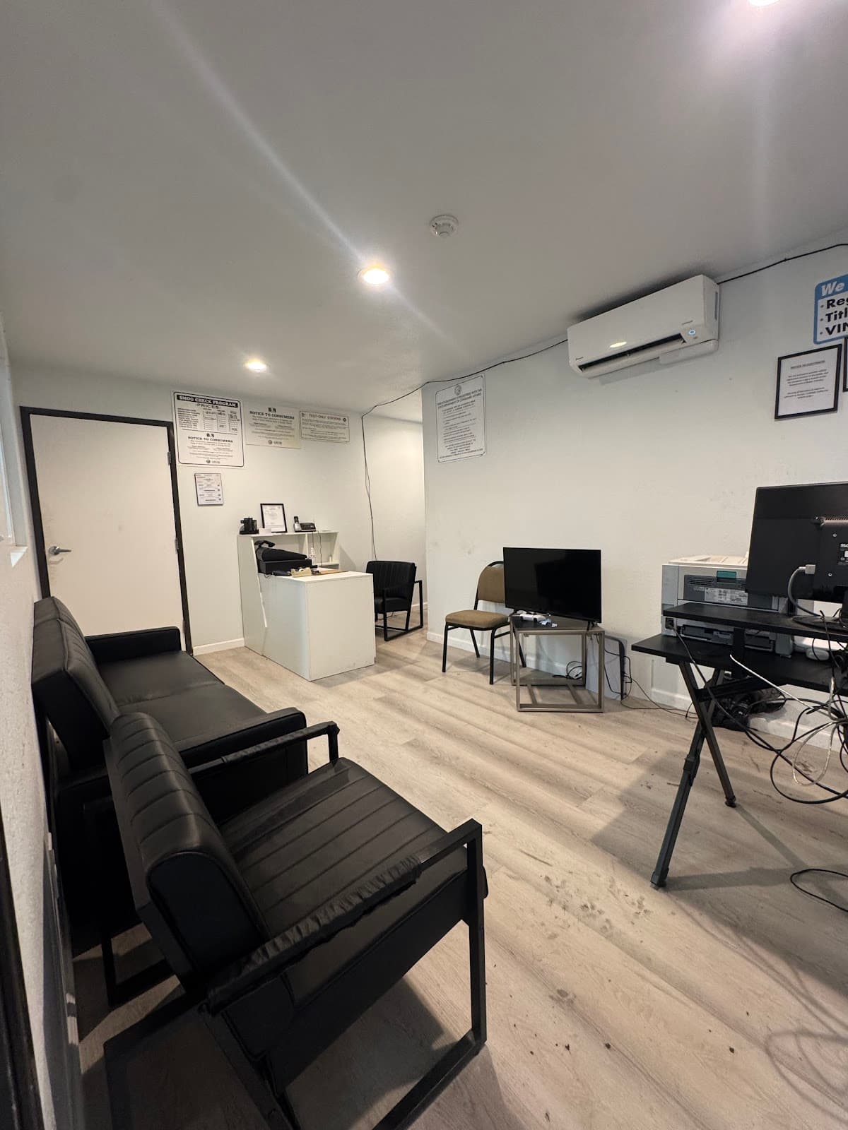 Waiting room with a black leather sofa and armchair, a television, and notices posted above the front counter